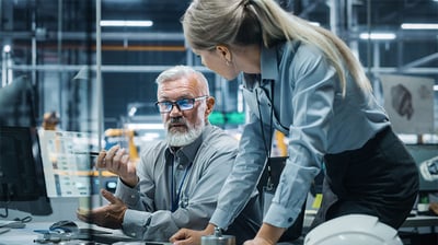 A photo of manufacturing employees discussing how AI and supply chain orchestration could boost their company's on-time delivery