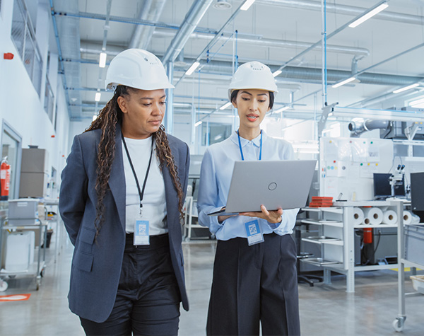 Two female manufacturing industry employees wearing hard hats walking in factory