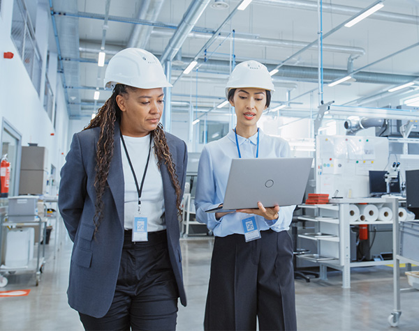 Two female manufacturing industry employees wearing hard hats walking in factory
