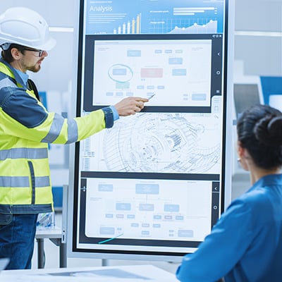 Photograph of industrial engineer talking with business leaders, and showing performance metrics from machine data.