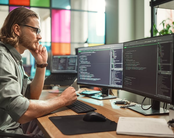 Photograph of an IT engineer looking at several computer monitors to determine how the shop floor data feeds into the OEE system.