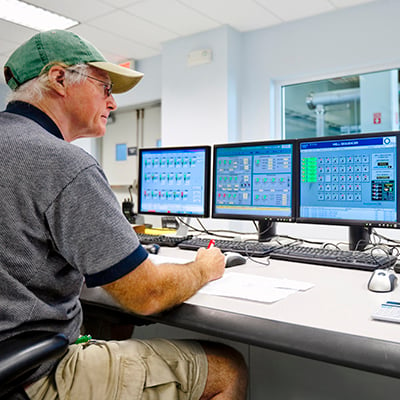 Photograph of an production engineer looking at several computer screens, using production metrics to improve manufacturing operational performance.