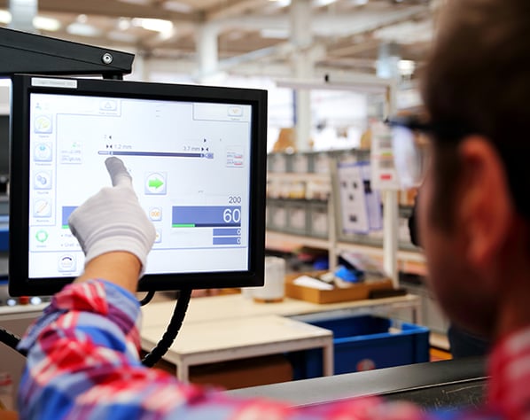 Photograph of manufacturing machine operator looking at computer screen to make decisions while looking at OEE and MES application.