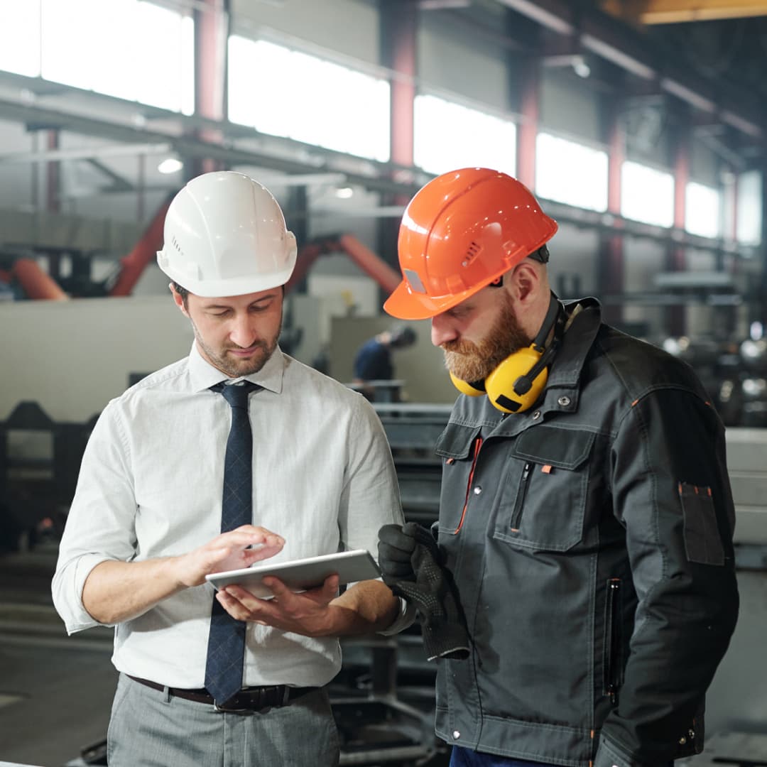 Two men in hard hats review a document on a factory floor